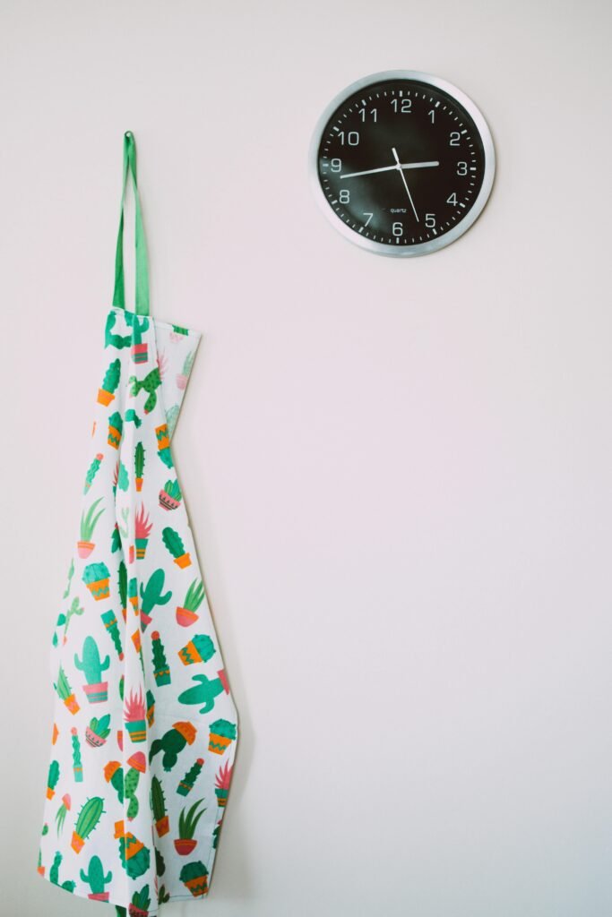 A minimalist kitchen wall featuring a colorful cactus-patterned apron and a modern clock.